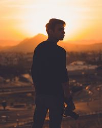 Rear view of silhouette man standing on mountain against sky during sunset