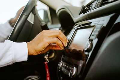 Side view of cropped unrecognizable african american male driver sitting in luxury car and setting radio for listening to music