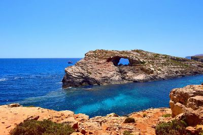 Rock formations by sea against clear blue sky