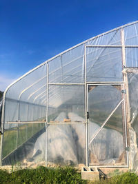 Scenic view of greenhouse in a green field against blue sky