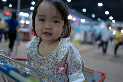 Portrait of baby girl sitting in shopping cart at supermarket