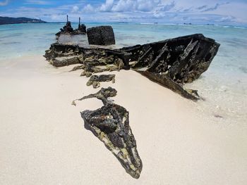 Damaged boat on shore at beach against sky