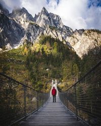 Rear view of person standing on footbridge against mountains