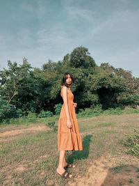 Young woman standing on field against sky