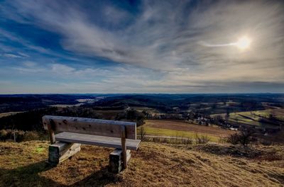 Empty bench on field against sky