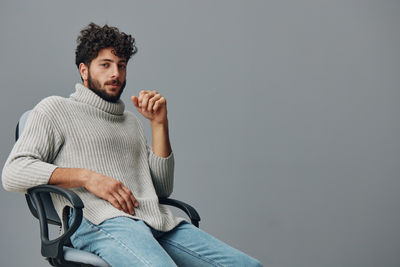 Young man sitting against white background