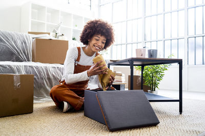 Smiling young woman using phone while sitting on floor