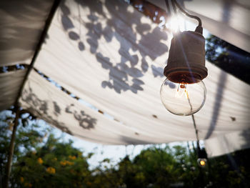 Low angle view of illuminated light bulb hanging from ceiling