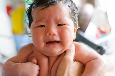 Cropped hand holding crying baby girl while taking bath