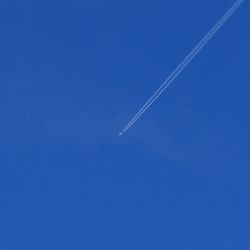 Low angle view of vapor trails in blue sky
