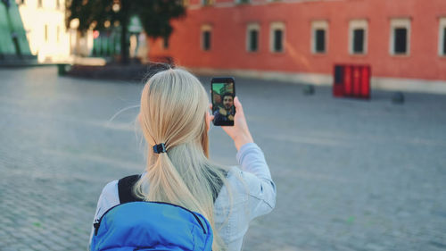 Rear view of woman photographing with mobile phone in city