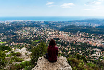 Rear view of woman sitting on rock against sky