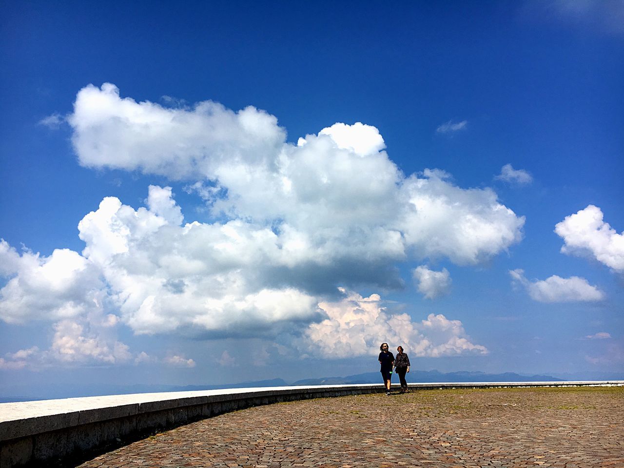 PEOPLE STANDING ON ROAD AMIDST LAND AGAINST SKY