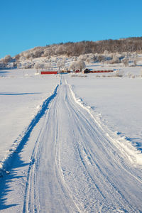 Snow covered road by land against blue sky