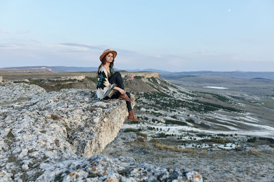 Full length of woman sitting on rock against sky