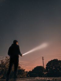 Rear view of silhouette man standing on field against sky at night