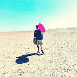 Rear view of woman walking on beach against clear sky