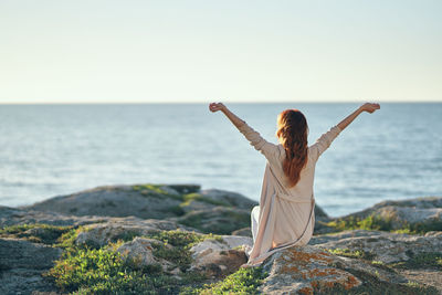 Rear view of woman standing on rock by sea against clear sky