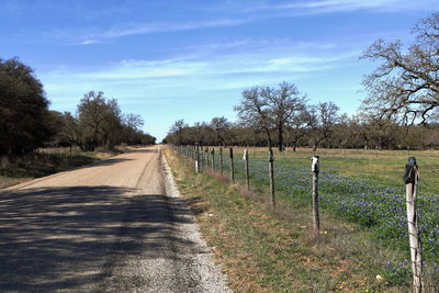 Empty road amidst field against sky