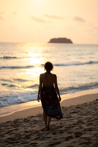 Rear view of woman walking on beach during sunset