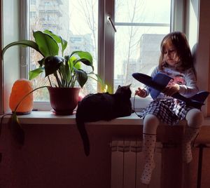 Full length of girl with model airplane sitting on window sill at home