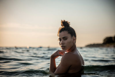 Portrait of shirtless man looking at sea against sky during sunset