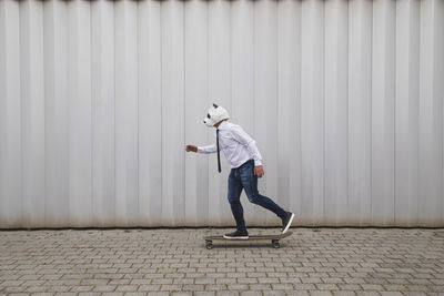 Side view of man skateboarding on footpath against wall