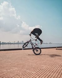 Man bmx cycling on promenade in city against blue sky