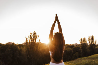 Rear view of woman with arms raised against sky during sunset