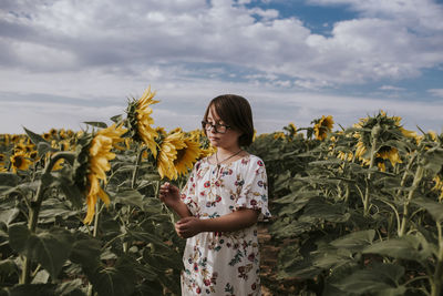 Girl standing in sunflower field against sky