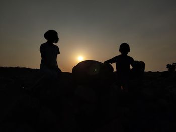 Silhouette people on field against sky during sunset