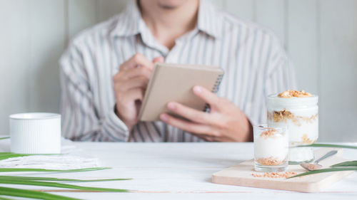 Midsection of woman using smart phone while sitting on table