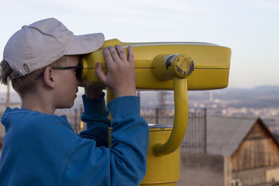 Boy is looking into big iron binocular on mountain viewpoint. travelling in beautiful places.