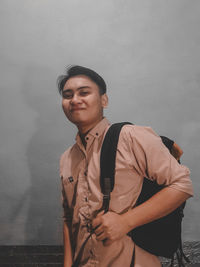 Young man looking away while standing against wall