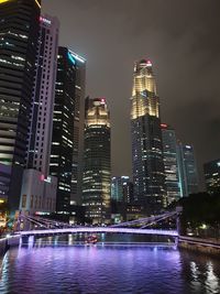 Illuminated buildings by river against sky at night