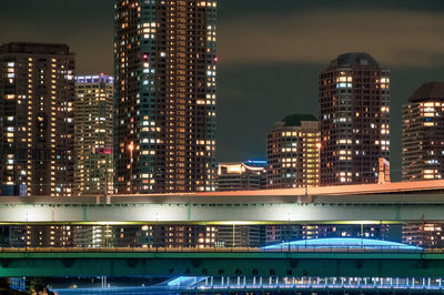 Illuminated modern buildings in city against sky at night