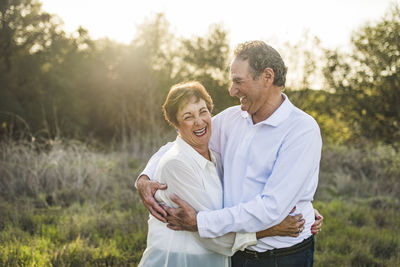 Senior couple hugging and laughing outside in backlight