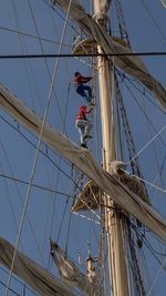 Low angle view of man working on rope against sky