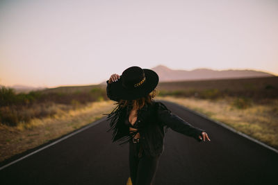 Woman in black hat and fringe dancing the street at sunset