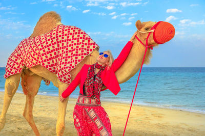 Woman with camel standing at beach against sky