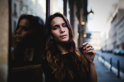 Portrait of young woman holding cigarette while leaning on window