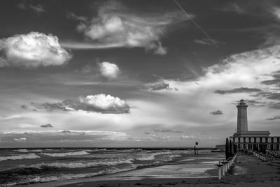 Lighthouse by sea against cloudy sky