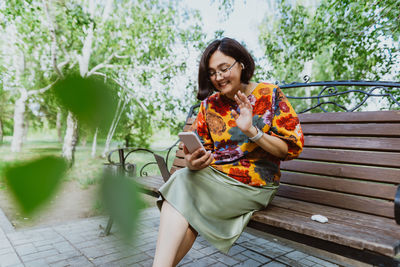 Cheerful adult lady with glasses engaged phone conversation while seated in park