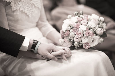 Midsection of bride with bouquet holding hand of bridegroom