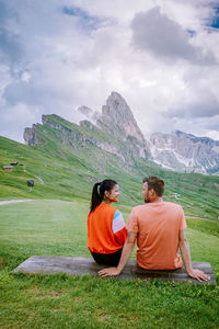 Rear view of couple sitting on mountain against sky