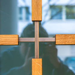 Reflection of man photographing glass window with wooden cross shape