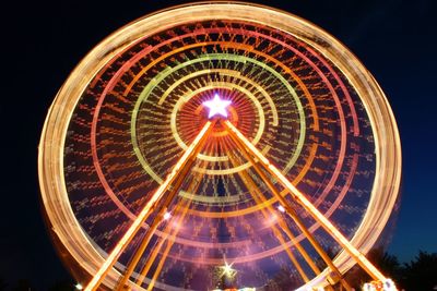 Light trail of spinning illuminated ferris wheel against sky