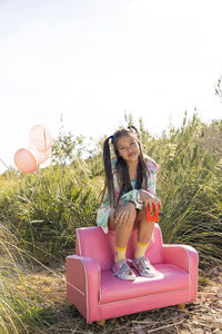 Girl holding toy camera sitting on pink armchair