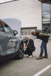 Saleswoman explaining about wheel to male customer while crouching near car