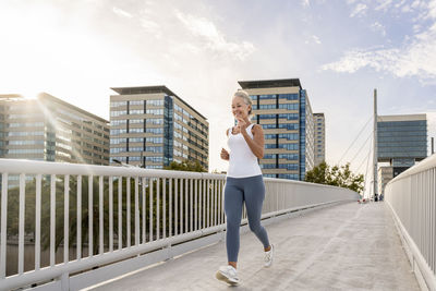 Mature woman jogging on footbridge in city